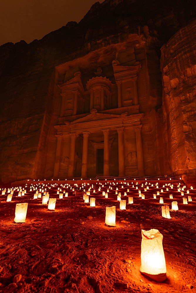 Exterior view of the rock caves and architecture of the facade in sandstone at Al Khazneh or The Treasury at Petra, Jordan at night, A red glow with small glowing lamps on the ground, Petra, Jordan