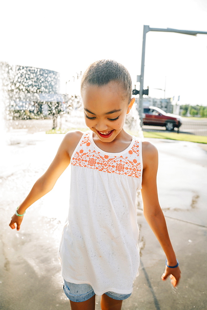 Smiling girl playing in public fountain in summer, United States of America