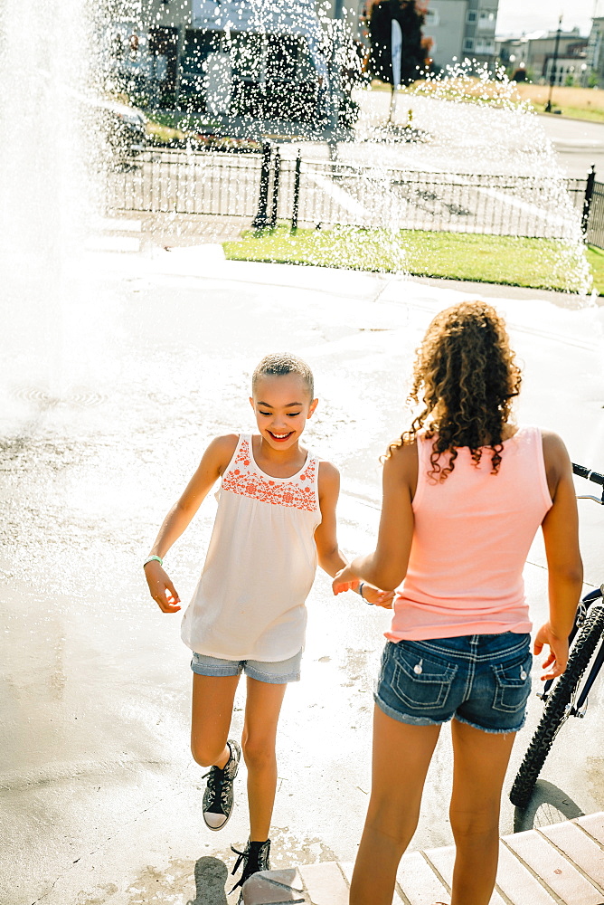 Smiling girls playing in public fountain in summer, United States of America