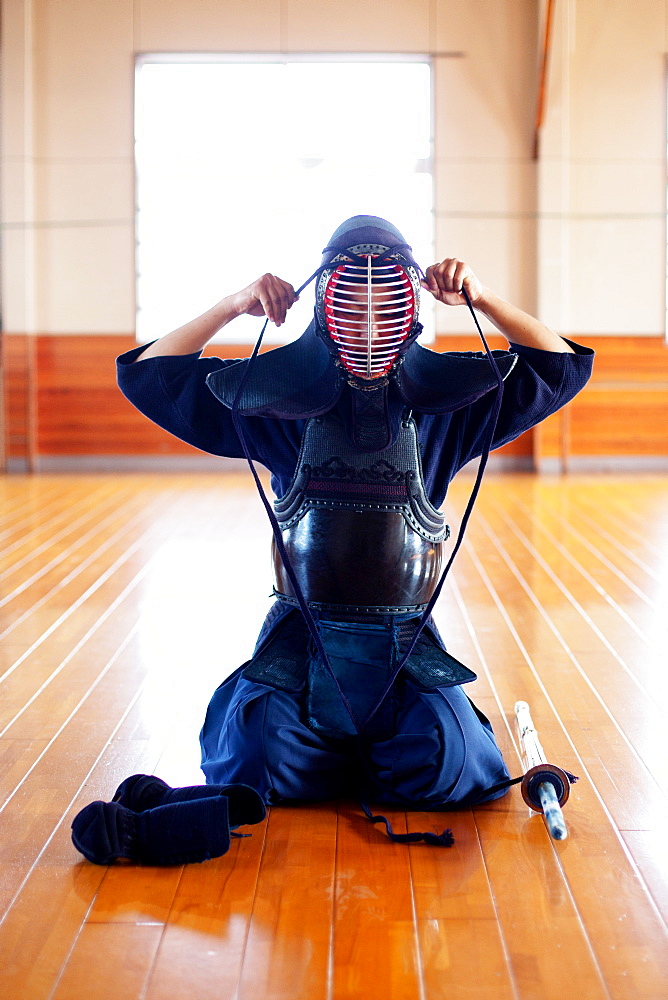 Female Japanese Kendo fighter kneeling on wooden floor, fastening Kendo mask, Kyushu, Japan