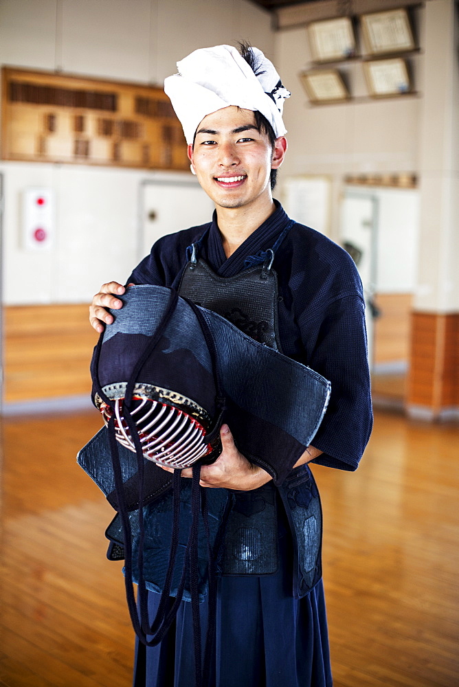 Male Japanese Kendo fighter standing in a gym, holding Kendo mask, looking at camera, Kyushu, Japan