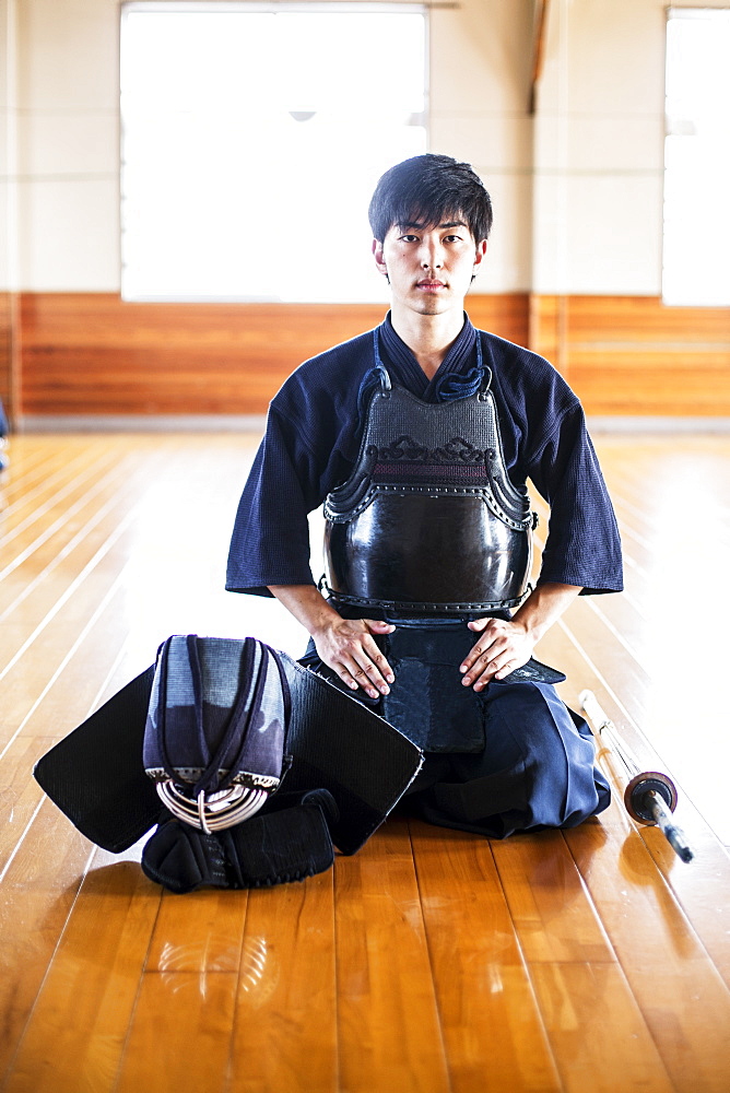 Male Japanese Kendo fighter kneeling on wooden floor, looking at camera, Kyushu, Japan