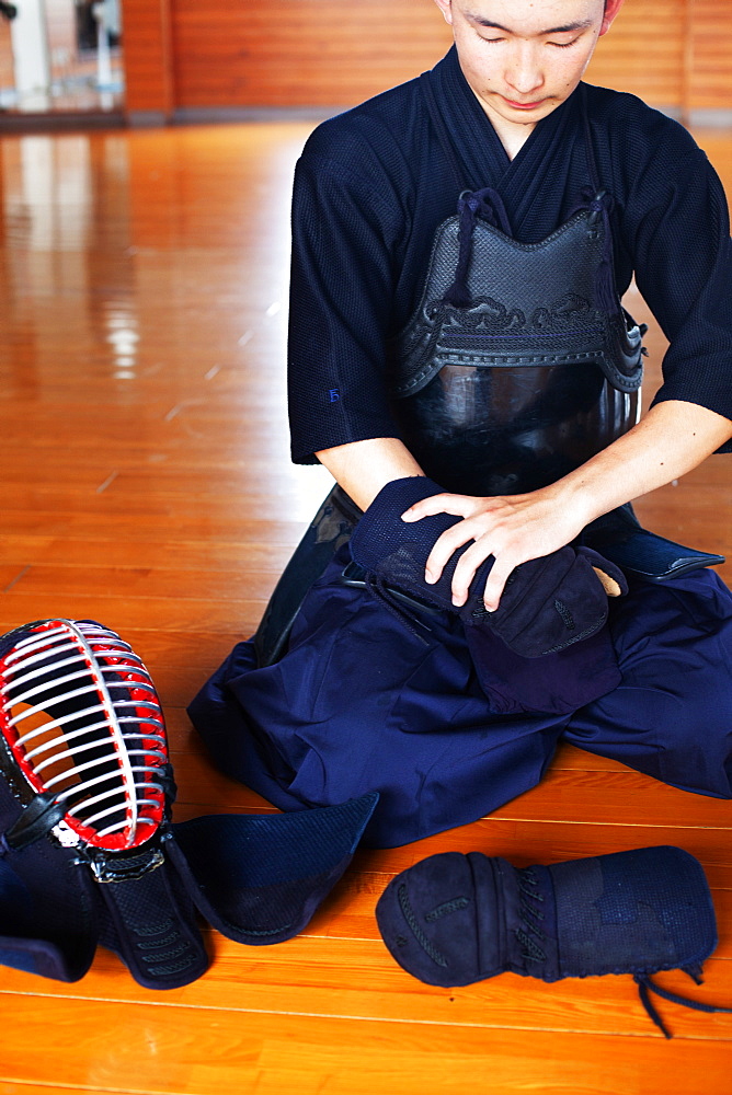 Male Japanese Kendo fighter kneeling on wooden floor, putting on Kote, hand protectors, Kyushu, Japan