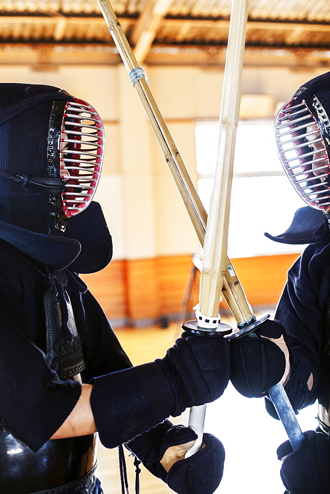 Two Japanese Kendo fighters wearing Kendo masks practicing with wood sword in gym, Kyushu, Japan