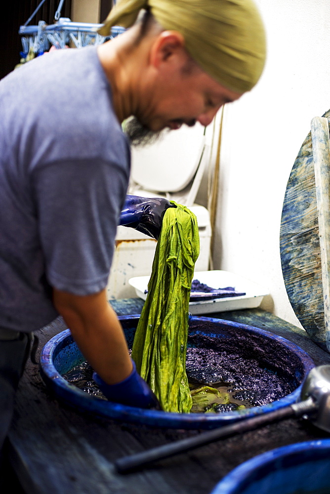 Japanese man wearing bandana standing in a textile plant dye workshop, dyeing piece of green fabric, Kyushu, Japan