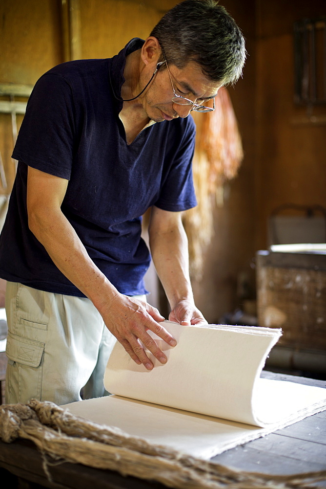 Japanese man standing in a workshop,  checking through sheets of traditional Washi paper, Kyushu, Japan