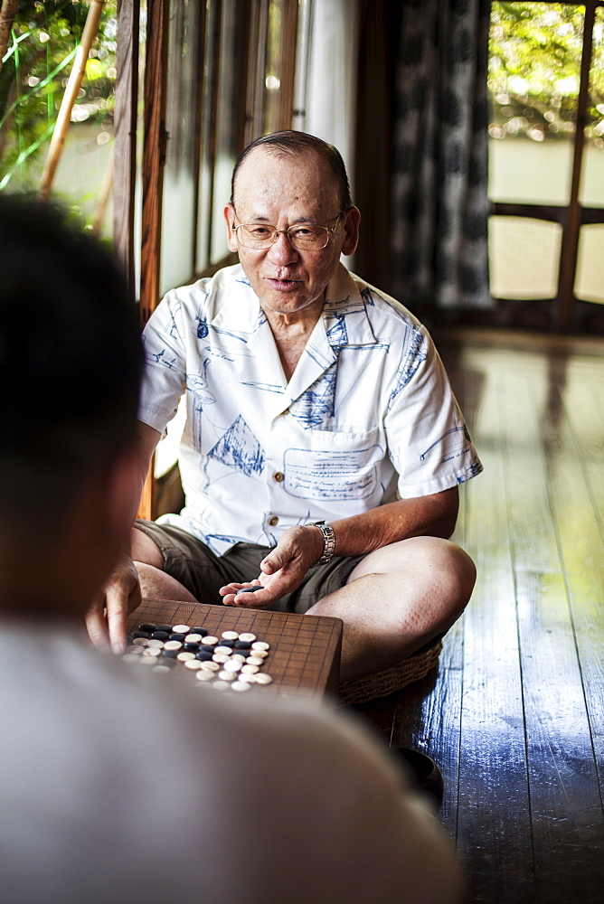 Two Japanese men sitting on floor on porch of traditional Japanese house, playing Go, Kyushu, Japan