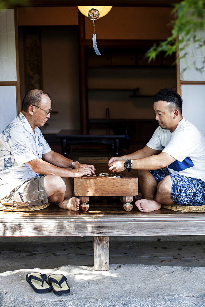 Two Japanese men sitting on floor on porch of traditional Japanese house, playing Go, Kyushu, Japan