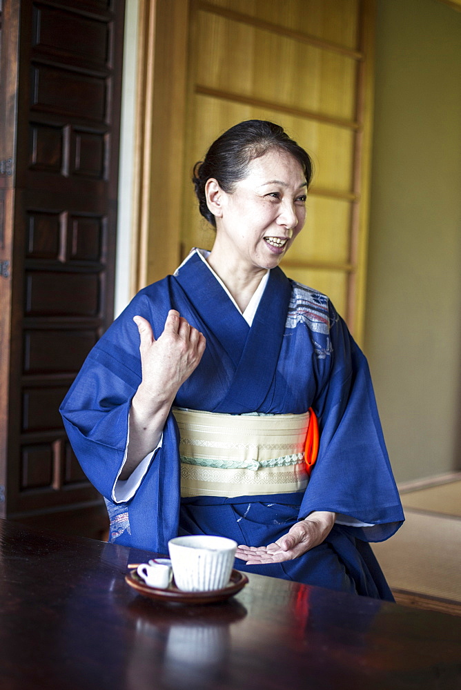 Smiling Japanese woman wearing blue kimono sitting on floor in traditional Japanese house, Kyushu, Japan