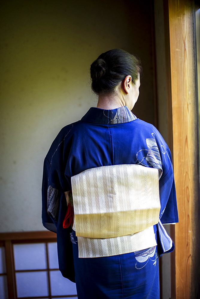 Rear view of Japanese woman wearing traditional bright blue kimono with cream coloured obi, Kyushu, Japan