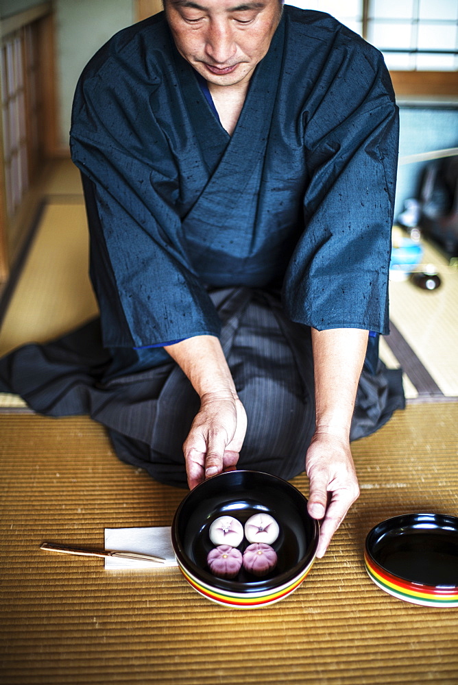 Japanese man wearing traditional kimono knelling on floor, holding a bowl with Wagashi, sweets traditionally served during a Japanese Tea Ceremony, Kyushu, Japan