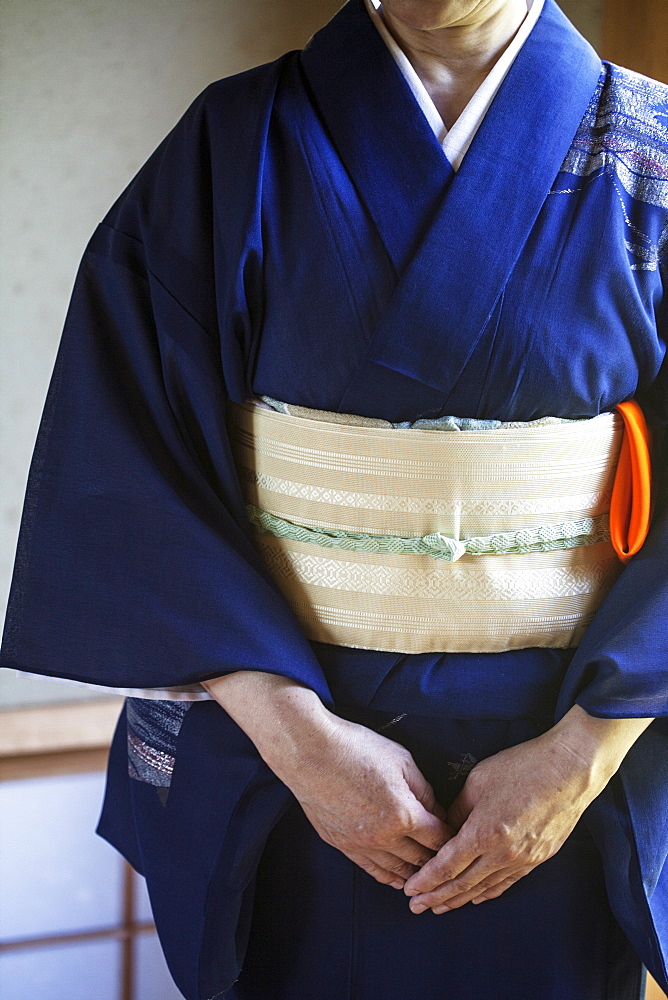 Close up of Japanese woman wearing traditional bright blue kimono with cream coloured obi kneeling on floor, Kyushu, Japan