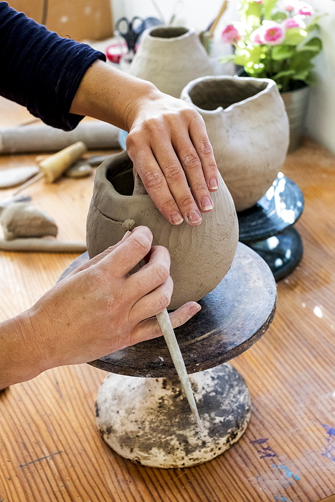 High angle close up of ceramic artist working on clay vase using pottery tool, England