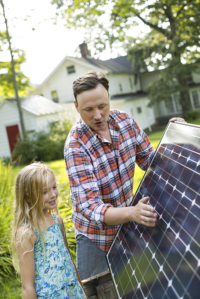 A man and a young girl looking at a solar panel in a garden.