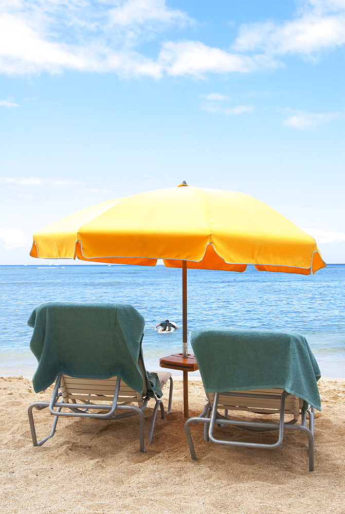 Lawn chairs and umbrella on beach, Honolulu, Oahu, USA