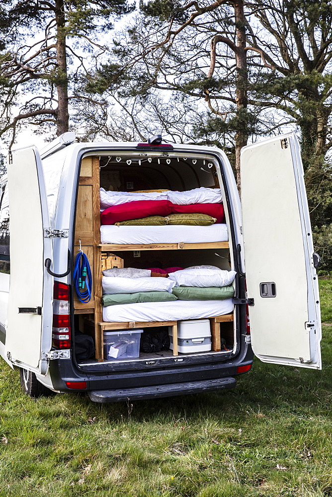 Rear view of camper van parked on a meadow, stacks of mattresses and bedding in back of vehicle, Oxfordshire, England