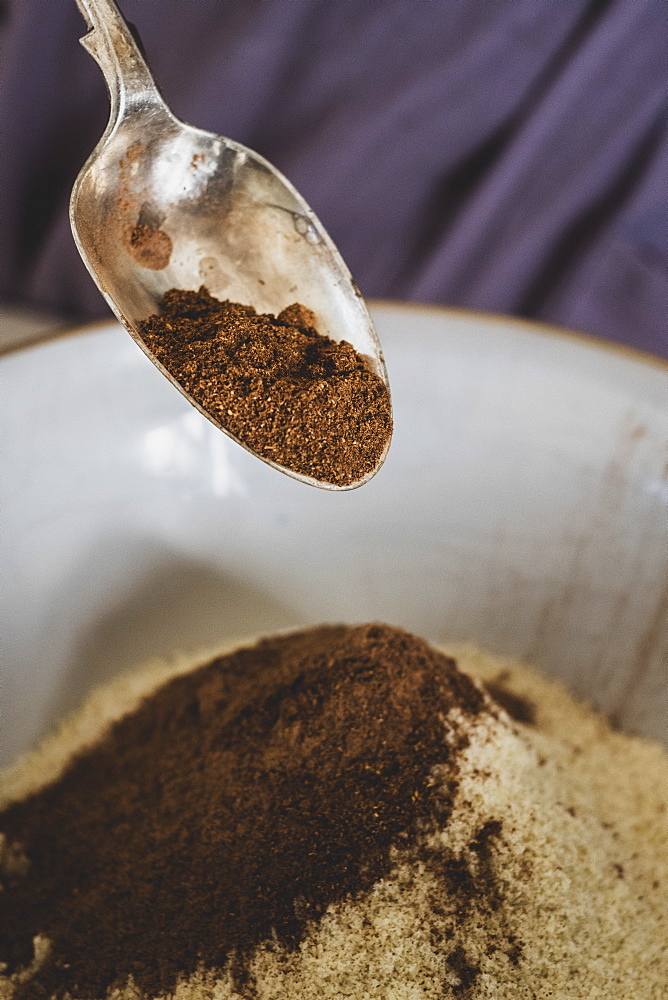 High angle close up of person pouring cocoa powder into mixing bowl with baking ingredients, England