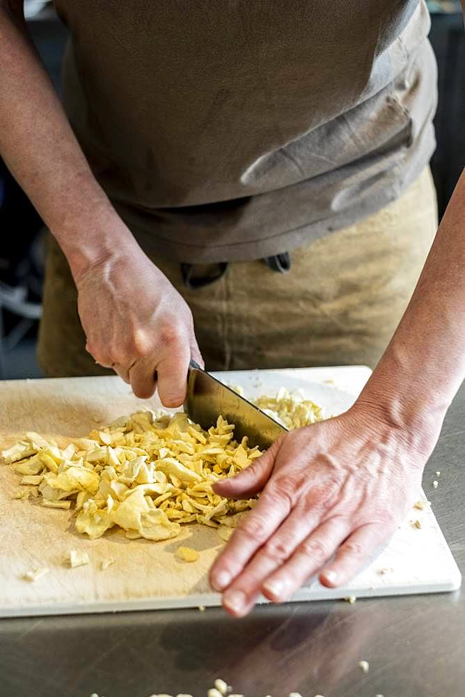 Close up of person standing in a kitchen, chopping dried apple slices with chef's knife