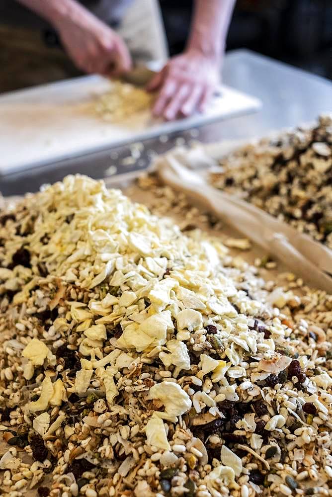 Close up of person standing in a kitchen, chopping food with chef's knife, heap of nuts, raisins and dried fruit in foreground