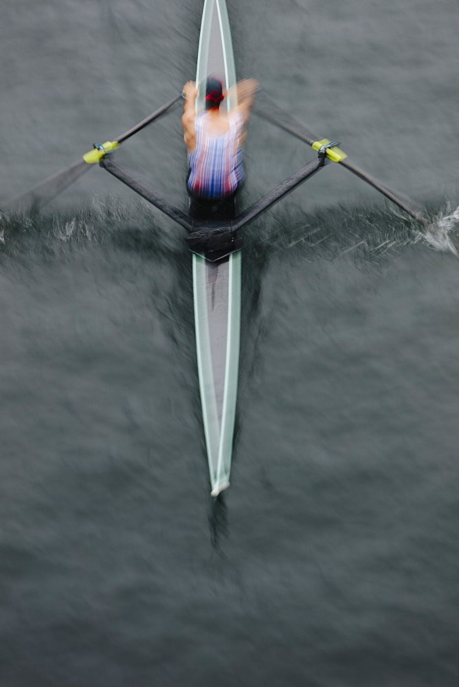 Overhead view of an oarsman in a single scull boat on calm water mid stroke, motion blur