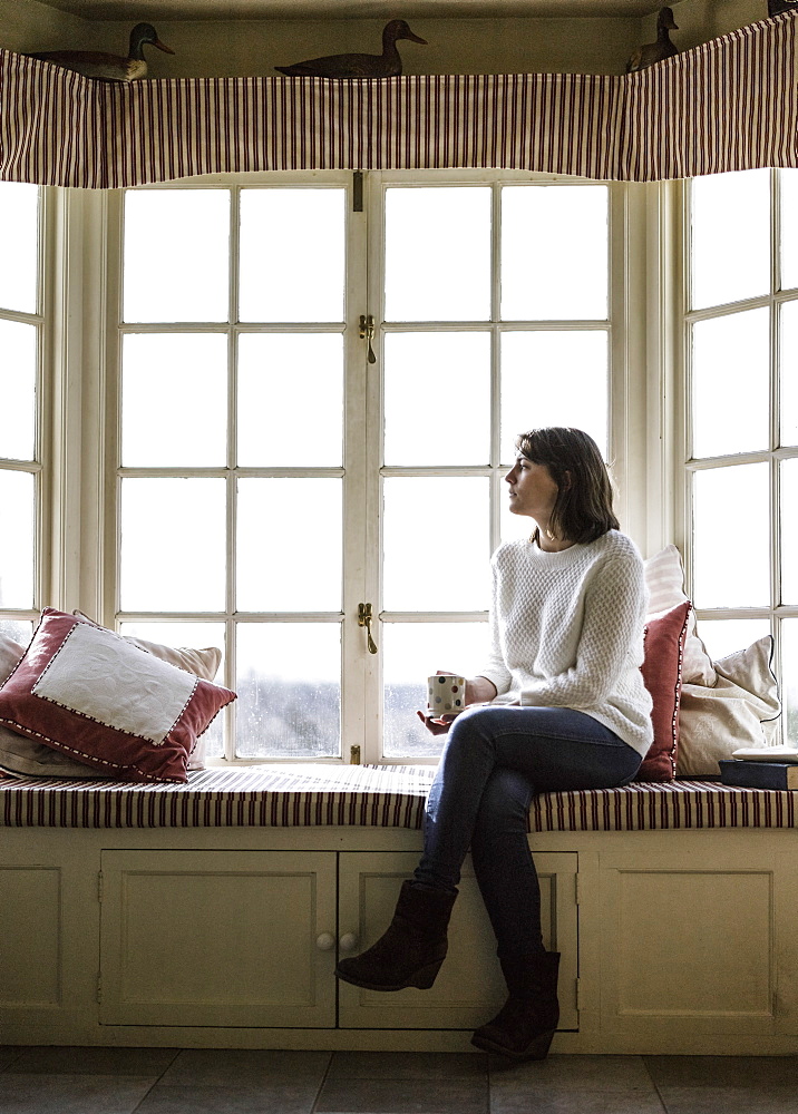 A young woman seated at a window seat, with a cup of tea, Ringwood, Hampshire, England