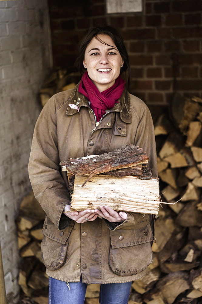 A woman carrying split logs for firewood from a large log store, Ringwood, Hampshire, England