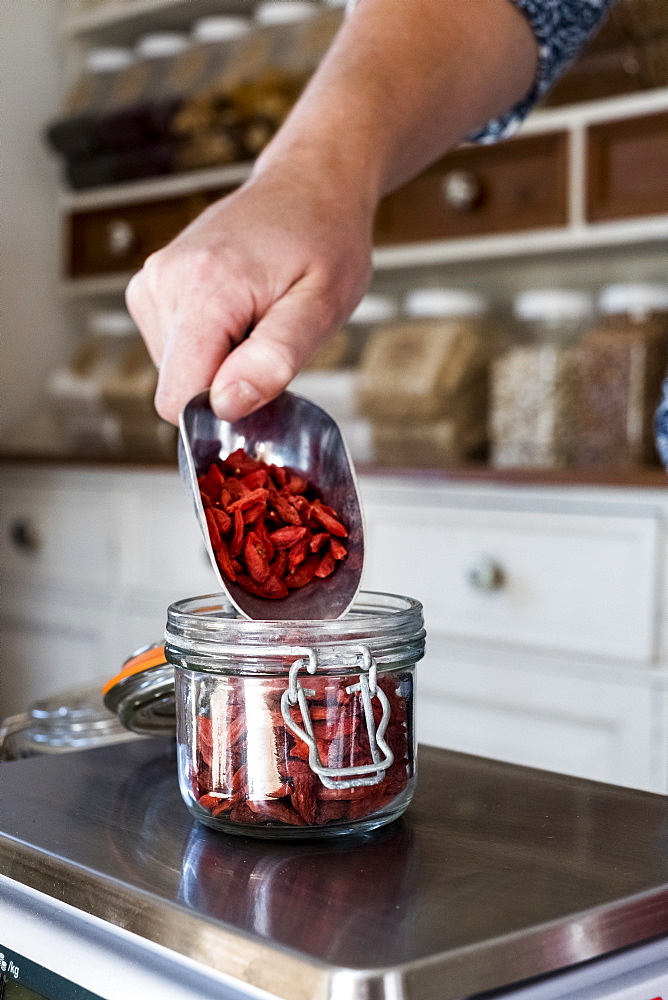 Close up of person weighing Goji berries in glass jar on kitchen scales