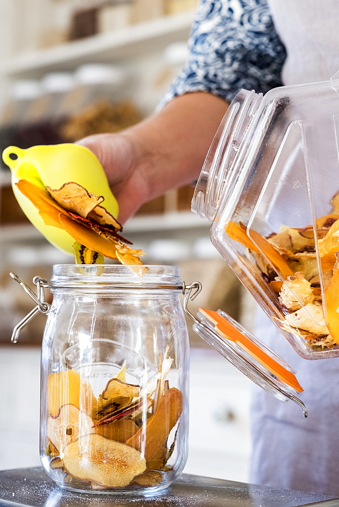 Close up of person standing in a kitchen, placing slices of dried fruit into glass jar