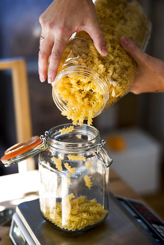 Close up of person pouring Fusilli pasta into glass jar on kitchen scales