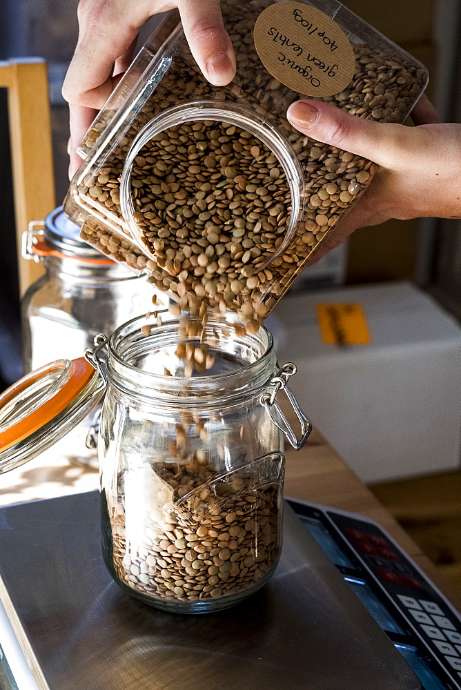 Close up of person pouring brown lentils into glass jar on kitchen scales