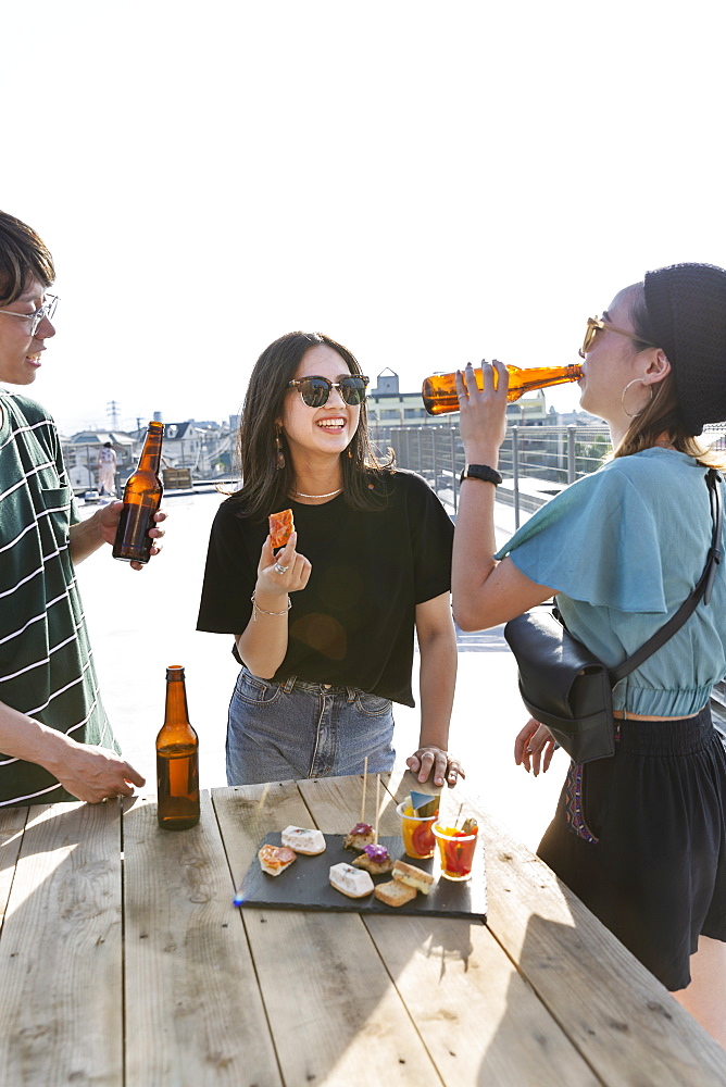 Young Japanese man and two women standing on a rooftop in an urban setting, drinking beer, Fukuoka, Kyushu, Japan