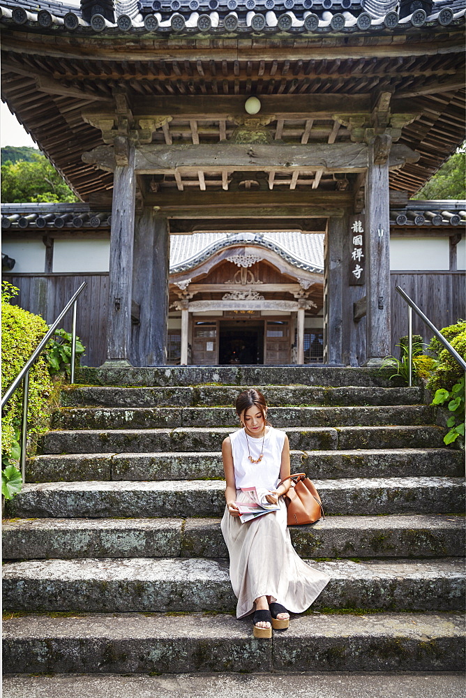 Japanese woman sitting on steps outside a Buddhist temple, Kyushu, Japan