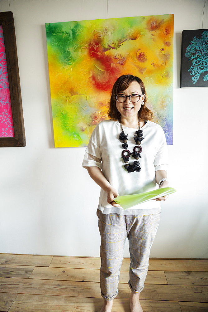 Japanese woman standing in front of abstract painting in an art gallery, smiling at camera, Kyushu, Japan