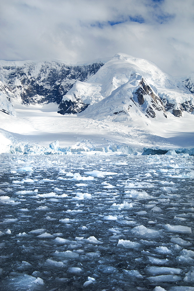 Mountains and snowy landscape reflected in calm sea water. Ice floes on the water, Antarctica