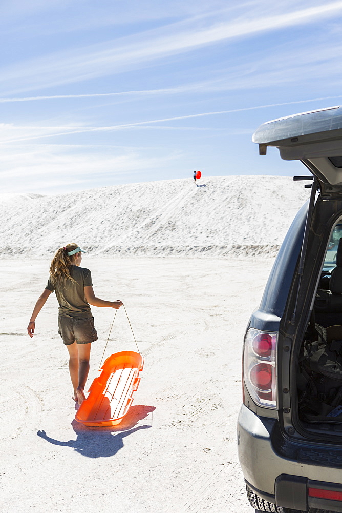 Teenage girl with a sled on white sand dunes, White Sands National Monument, New Mexico, United States