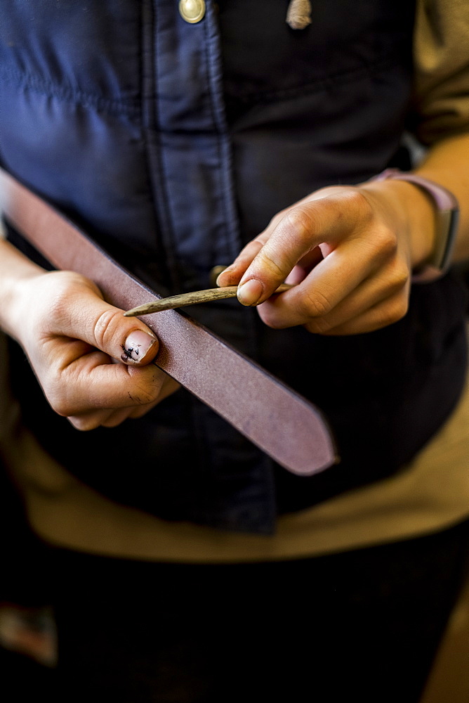 Close up of female saddler standing in workshop, working on leather strap, Berkshire, United Kingdom