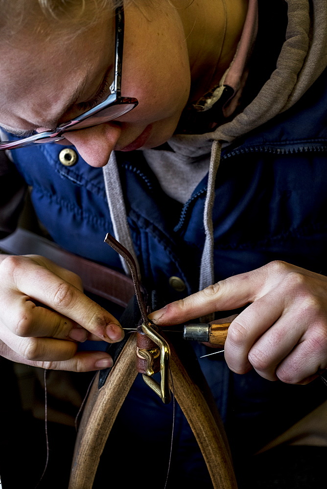 Close up of female saddler standing in workshop, working on leather strap, Berkshire, United Kingdom