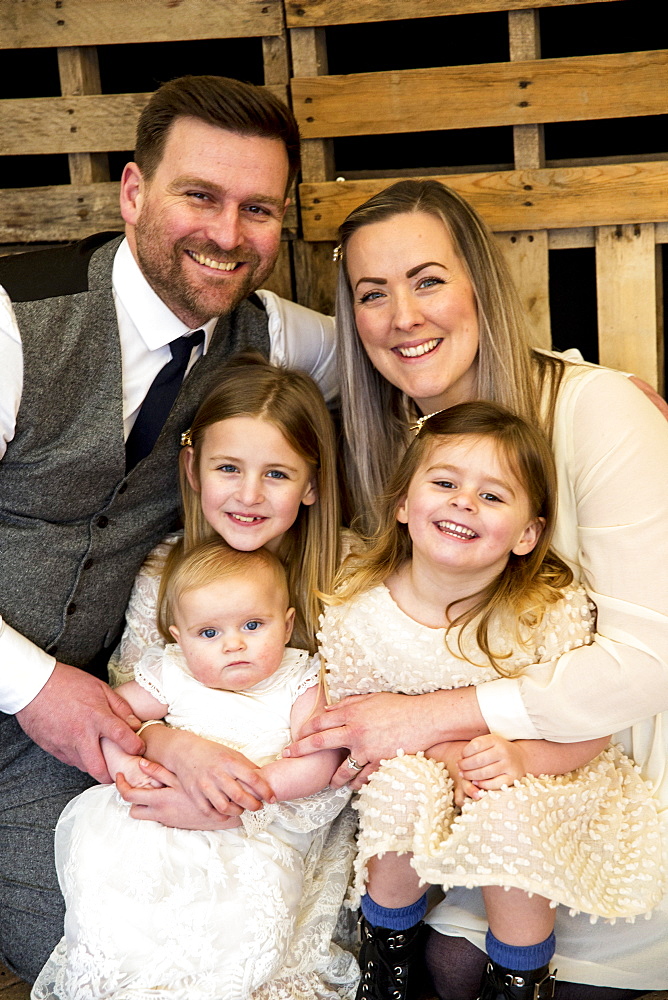 Portrait of smiling parents with their three young daughters during naming ceremony in an historic barn