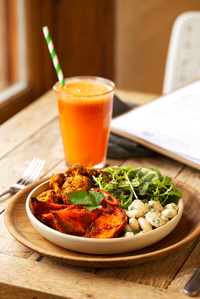 High angle close up of glass of carrot juice and bowl of mixed vegetables in a cafe