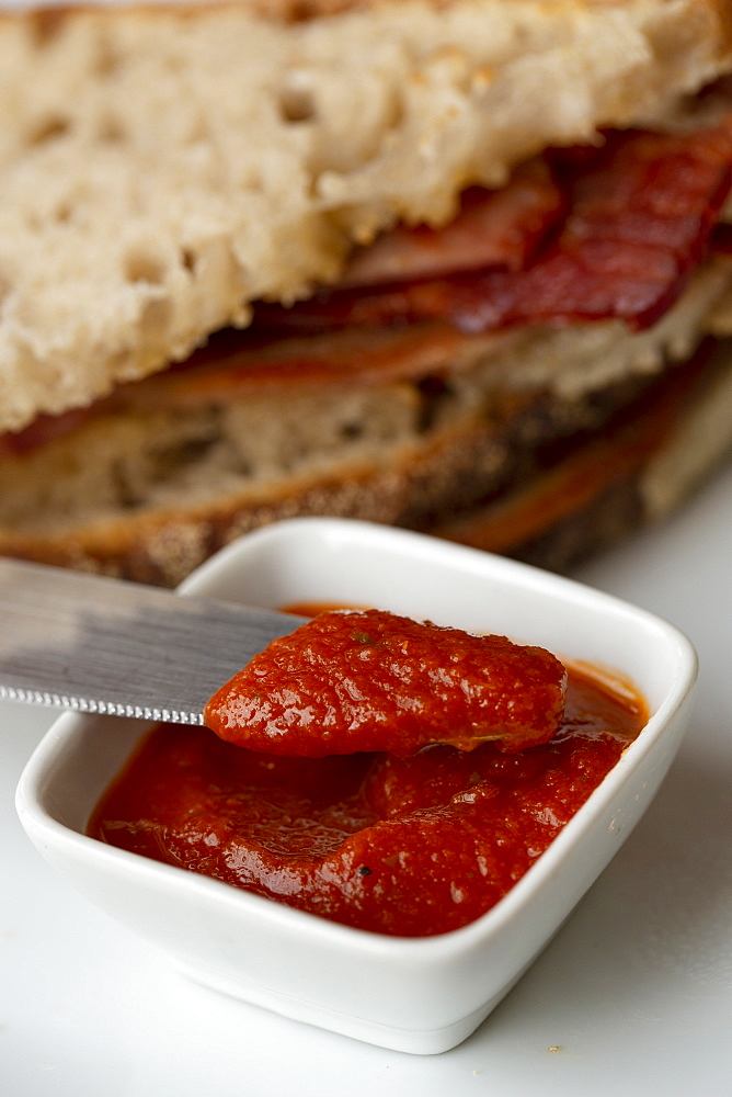 Close up of bacon sandwich and small bowl of home made tomato sauce in a cafe