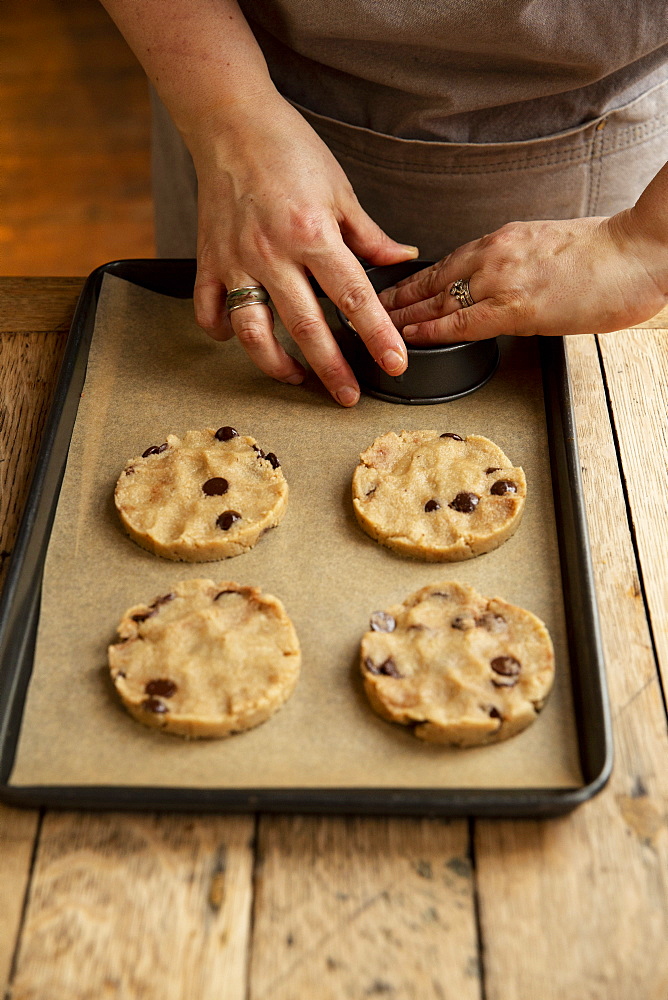 High angle close up of person standing at wooden table, baking chocolate chip cookies