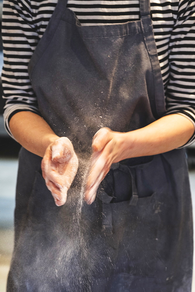 Artisan baker in apron patting her hands with flour