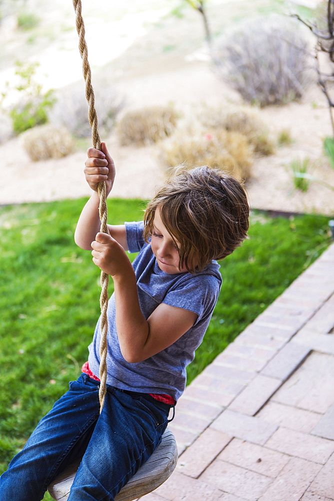 Six year old boy using a rope swing on a wide porch in the shade