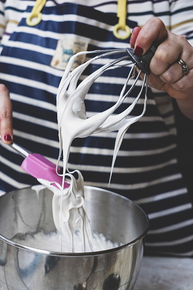 A woman making meringues whipping egg whites with a whisk