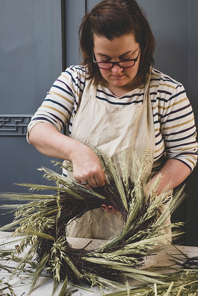 Woman making a winter wreath, adding dried grasses and seedheads and twigs with brown leaves