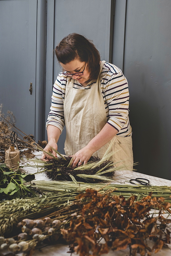 Woman making a winter wreath, adding dried grasses and seedheads and twigs with brown leaves