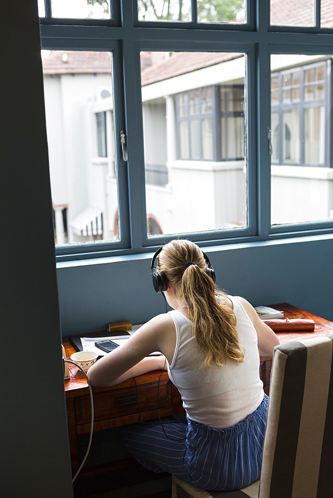 A thirteen year old girl wearing headphones doing homework seated in a quiet spot