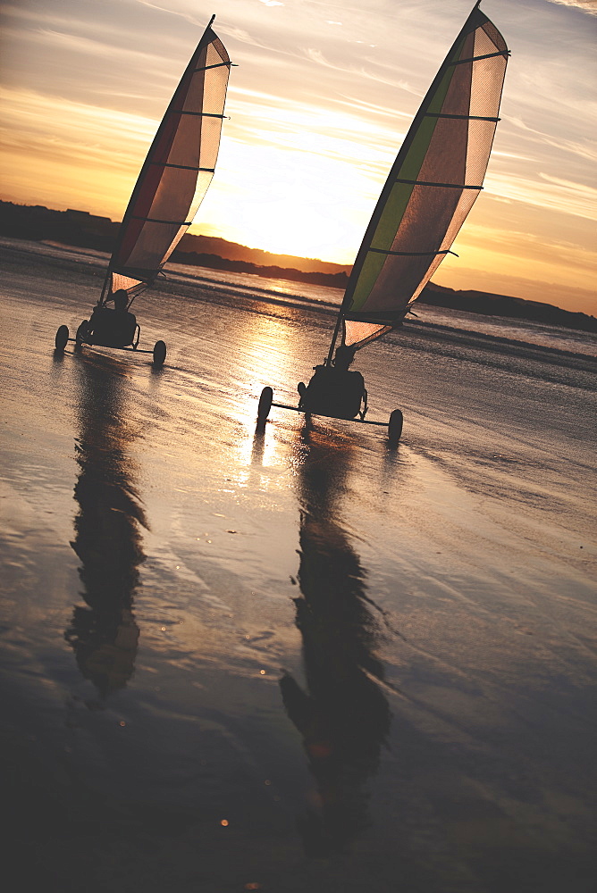 Two sand yachts racing along a sandy beach at sunset