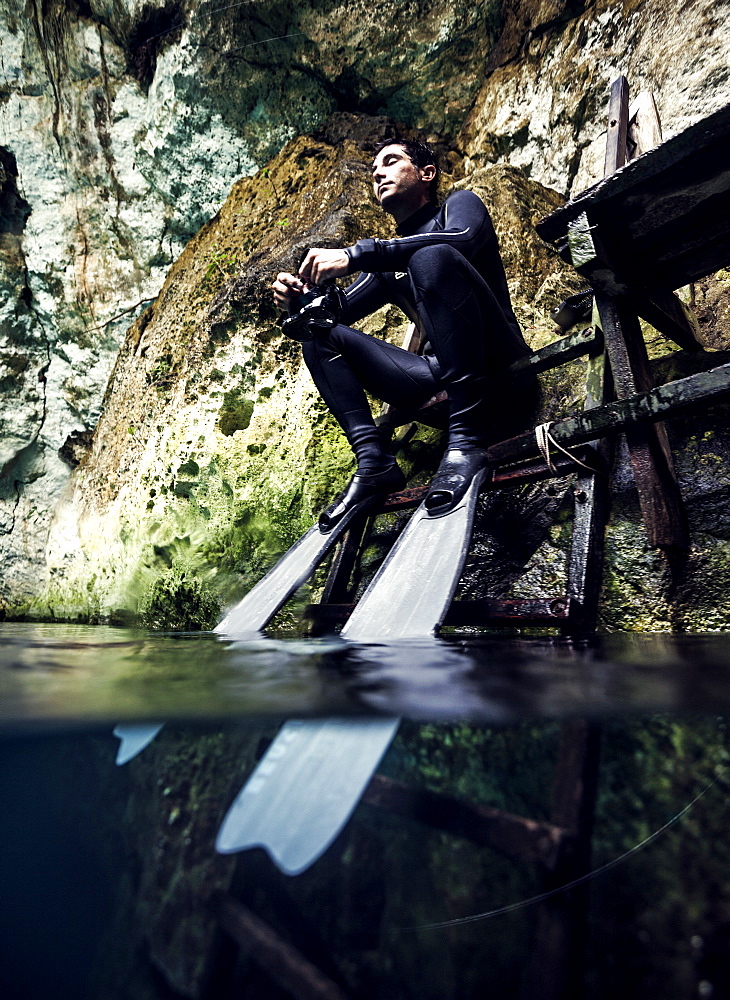 Man wearing wet suit and flippers sitting on a platform, rocks in background, United States of America