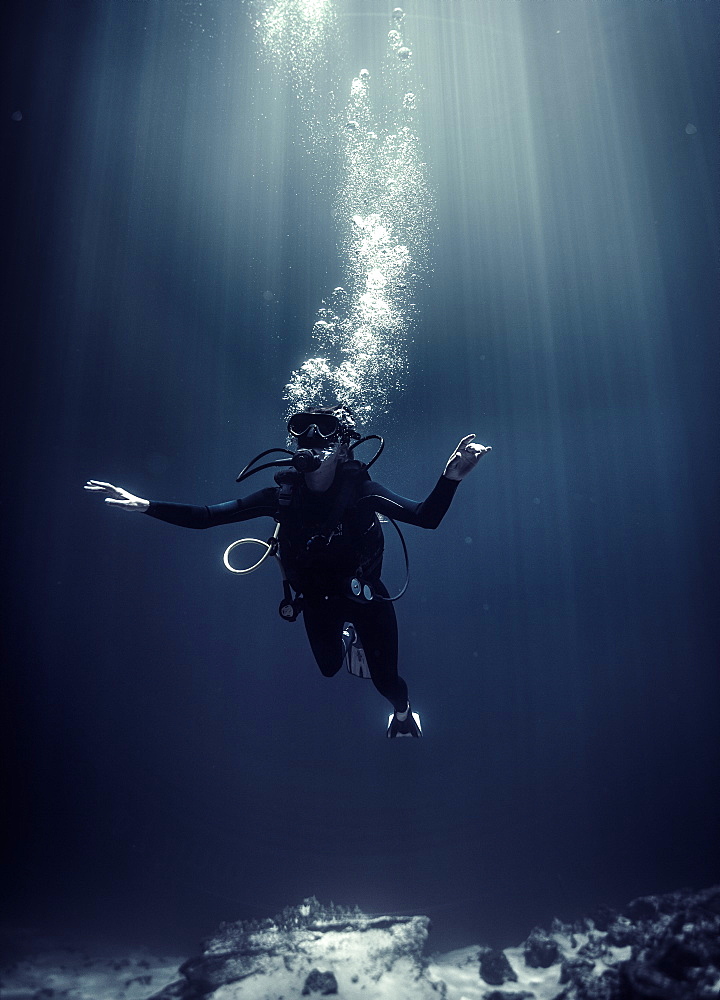 Underwater view of diver wearing wetsuit, diving goggles and oxygen cylinder, air bubbles rising, United States of America